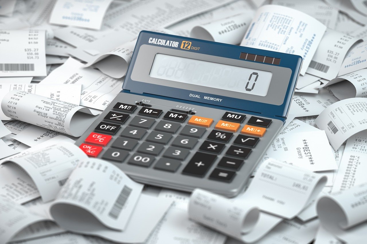 A person calculating taxes at a desk with a calculator, tax forms and a laptop, illustrating tax preparation.