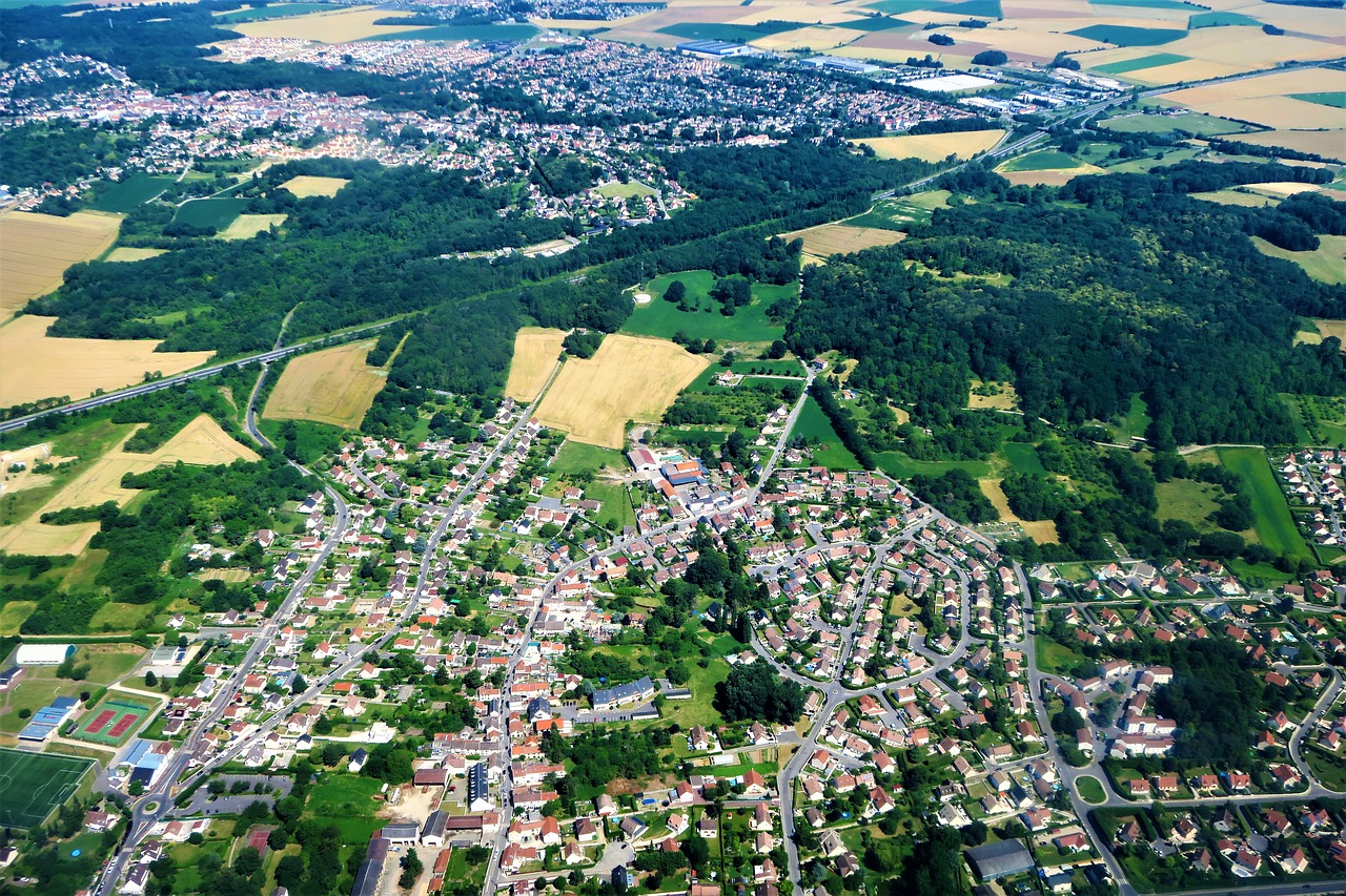 Aerial view showcasing a picturesque countryside town surrounded by lush greenery and winding roads.