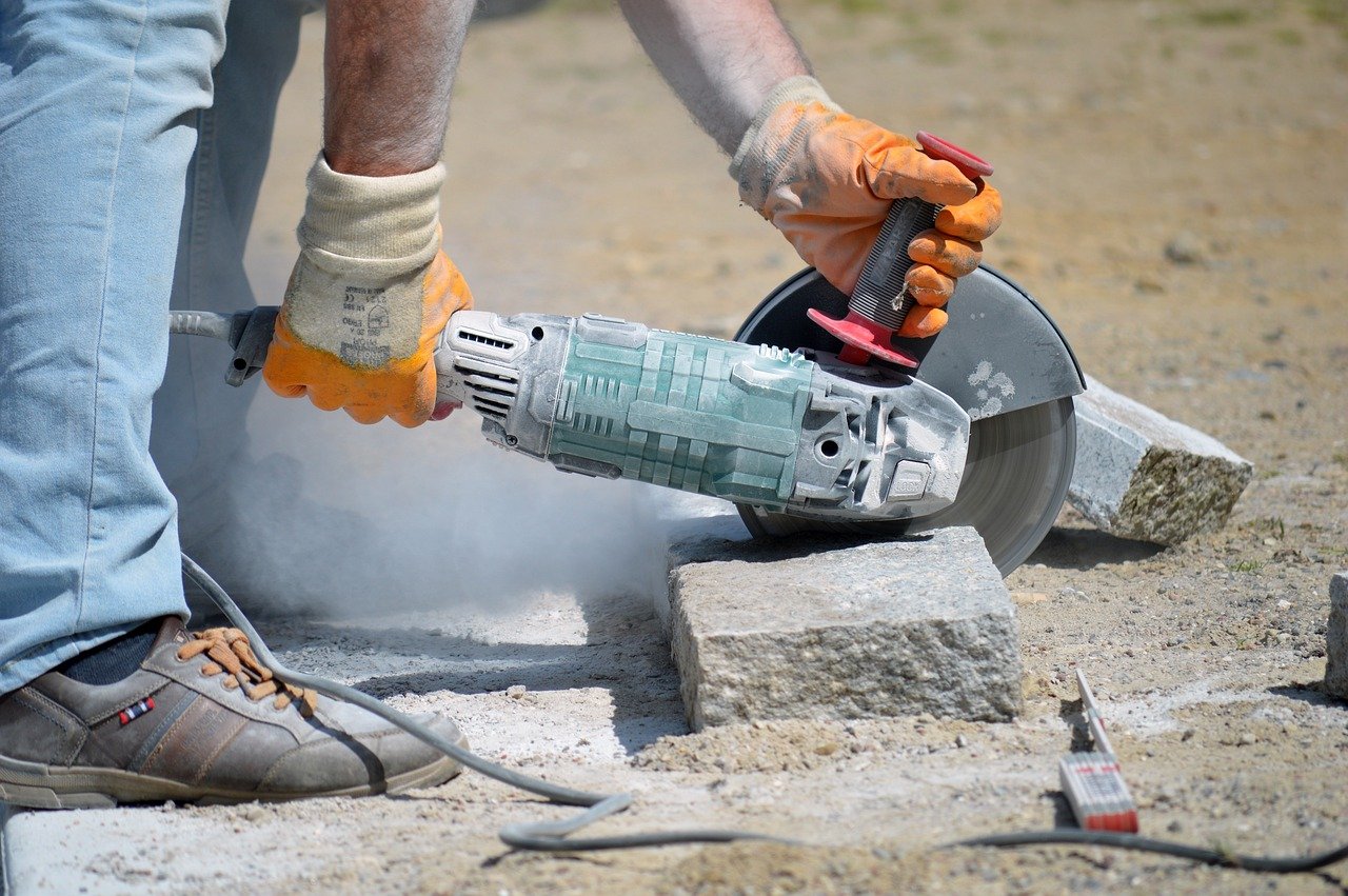 A man uses a concrete grinder, focused on cutting through a thick slab of concrete in a work environment.