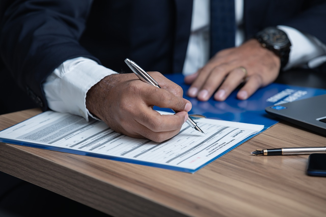 A man in a suit signs a document on a desk, showcasing professionalism and attention to detail.