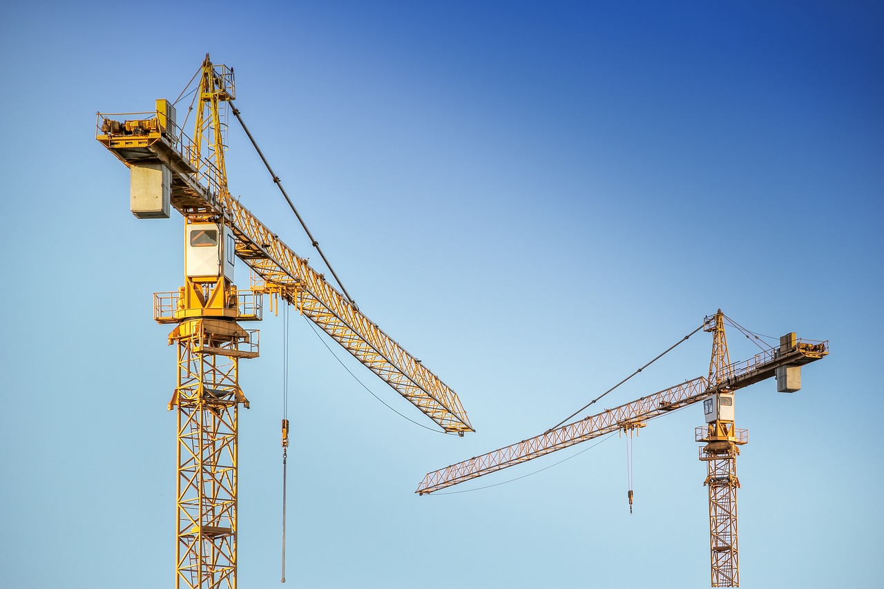 A pair of yellow construction cranes rise against a vibrant blue sky, illustrating the dynamic nature of urban development.