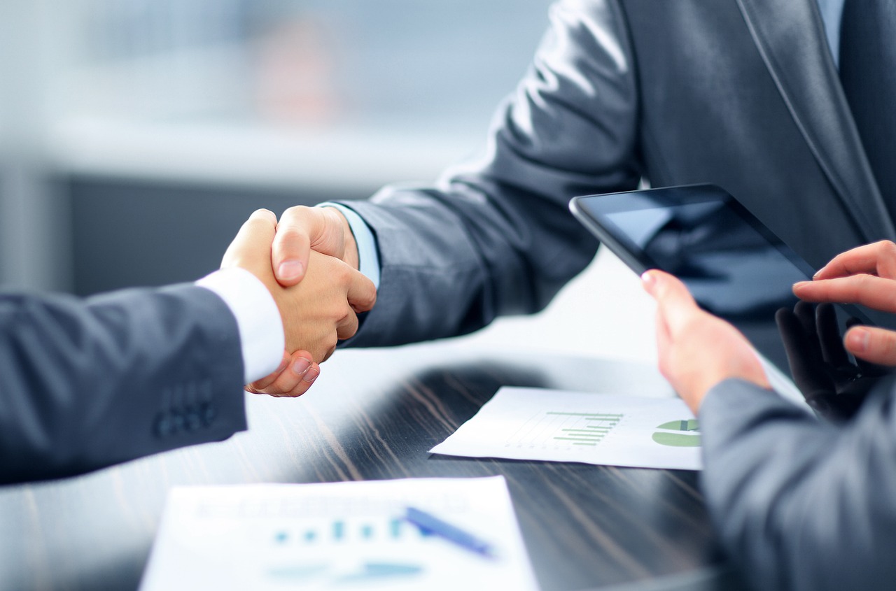 A handshake between two business individuals at a table, representing partnership and mutual understanding in a professional setting.